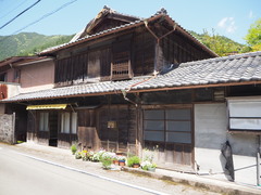 木造で2階建ての古い住宅を建物が面した道路の斜め横から撮影した写真