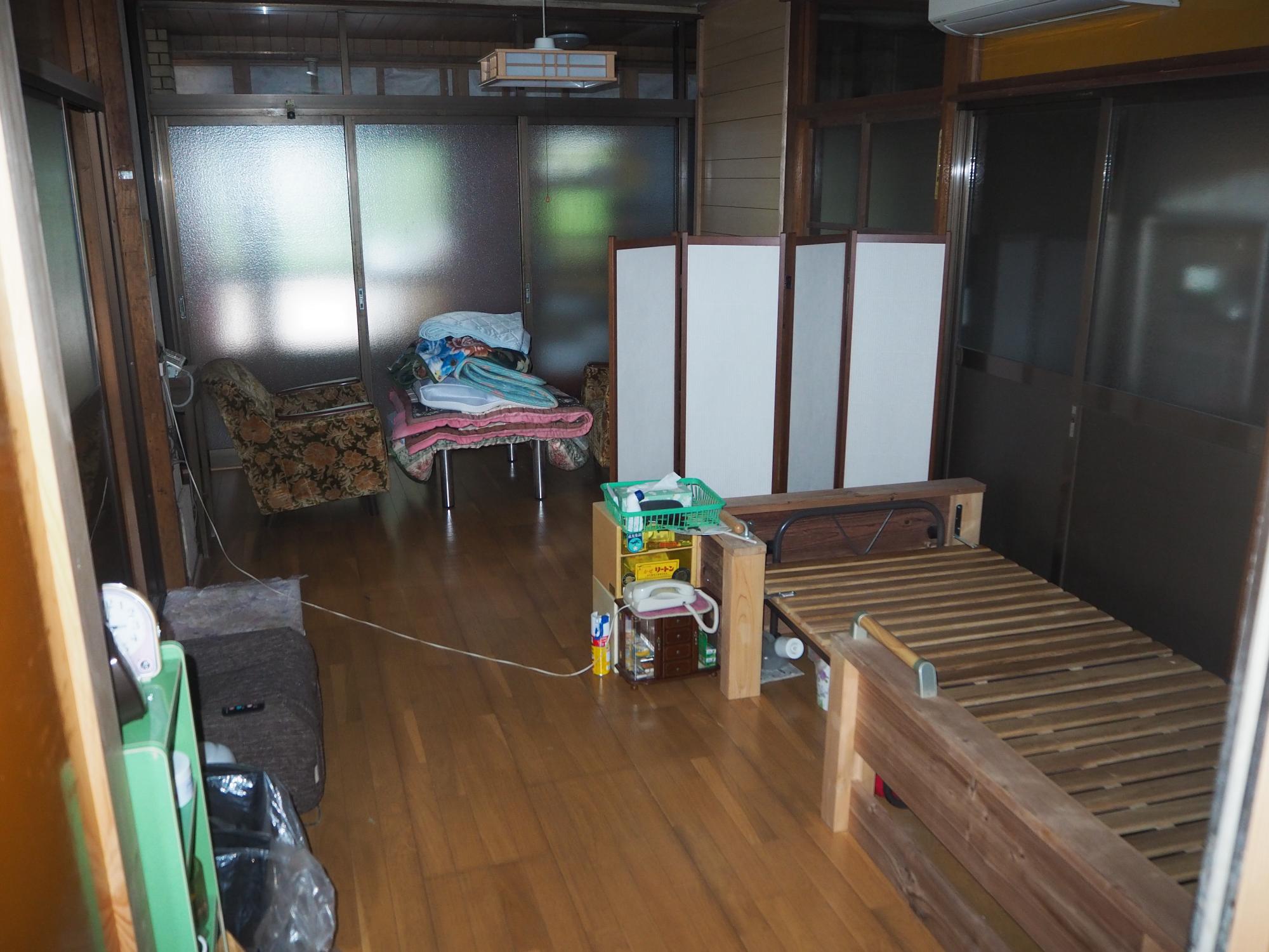 部屋の3面にガラス戸が設置され、部屋の右側にはベッドフレームが置かれている1階洋間の写真