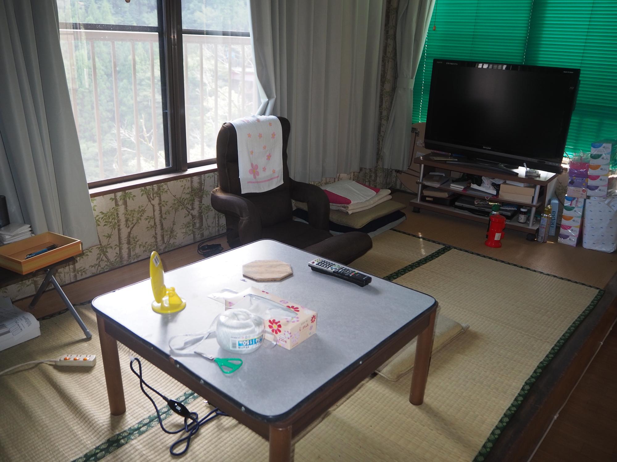 コタツ、座椅子、テレビが置かれ、左側に窓がある小上がりの写真