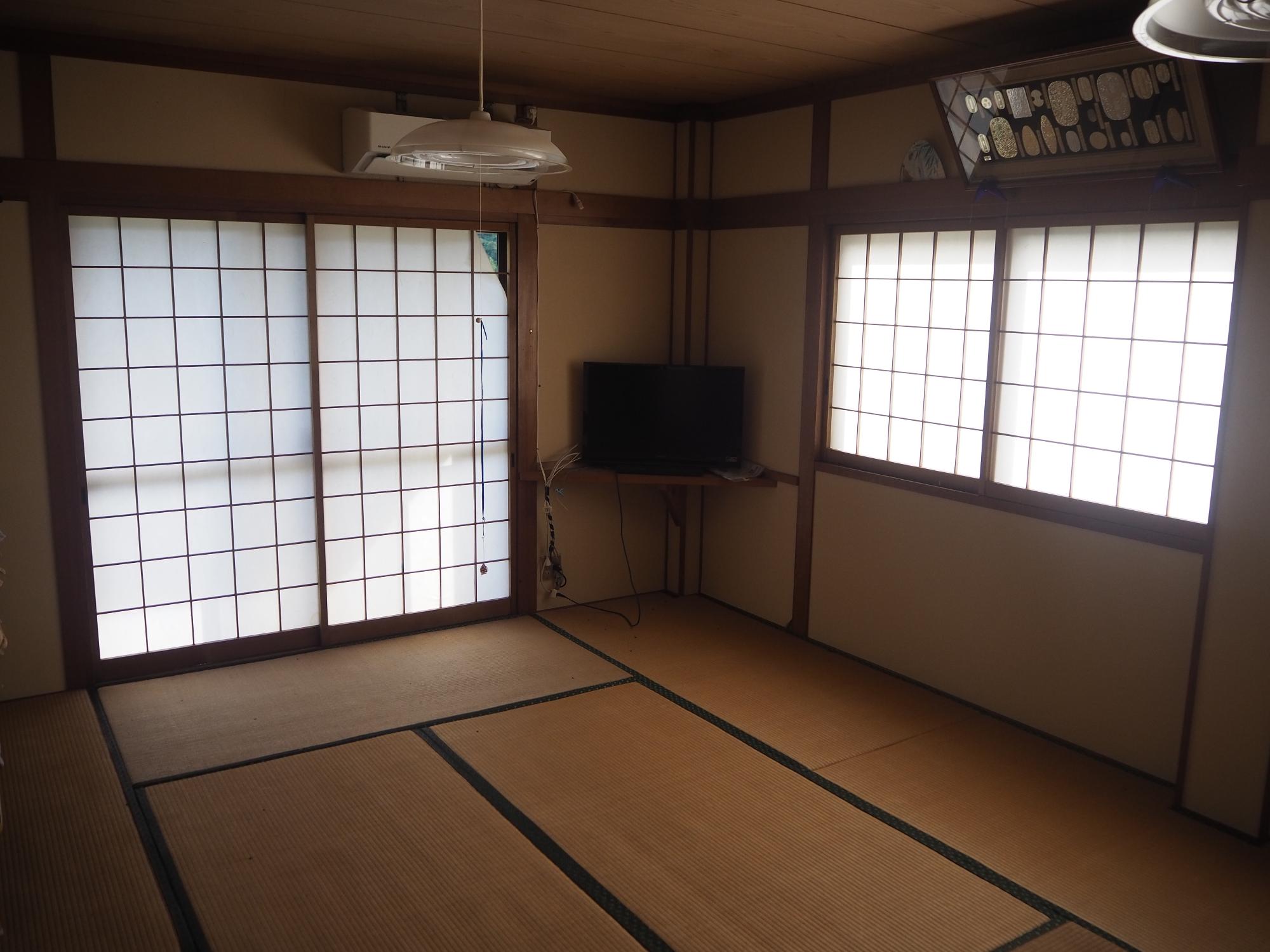 部屋のコーナーにテレビが置かれ、窓には障子戸が設置されている2階和室の写真