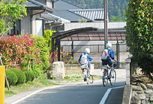 住宅街の道路をジャージ姿の子供2人が自転車に乗っている後ろ姿の写真